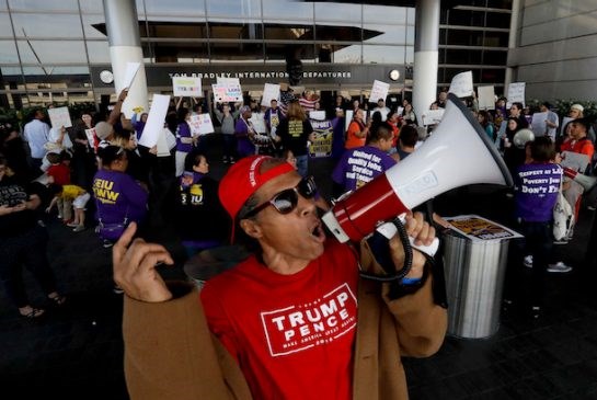 A supporter, foreground, of President Donald Trump yells as demonstrators chant at JFK on Monday. The ripple effects of new immigration restrictions are being felt as far away as Edmonton.