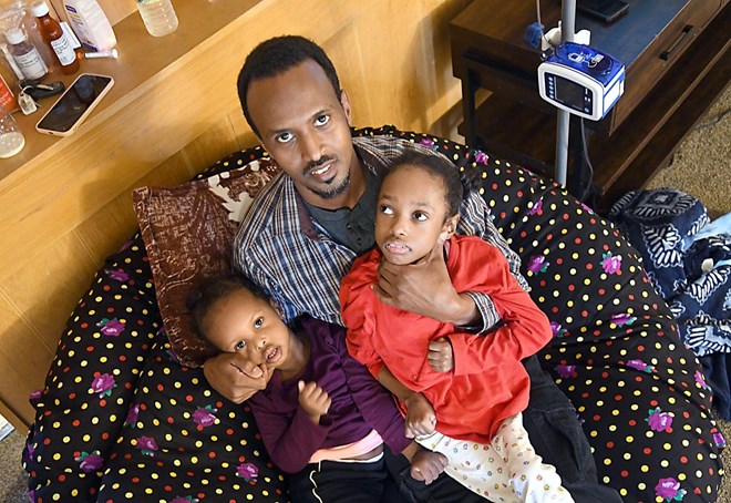 Ali Abdi supports the neck of his daughter, Ansal, wearing red, while cradling his daughter, Maryam, wearing purple. Both girls, and their younger sister, Asiya, have been diagnosed with a fatal form of the genetic disease leukodystrophy.Photo by Pat Christman