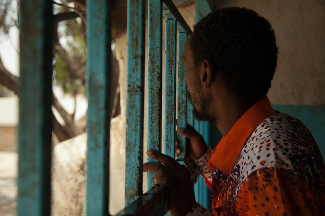 A patient looks out through the bars at the front of the mental health ward at the Hargeisa Group Hospital. Patients are kept locked in the ward, although they are allowed to move freely within the separate male and female sections of the facility. [Zoe Flood/Al Jazeera]