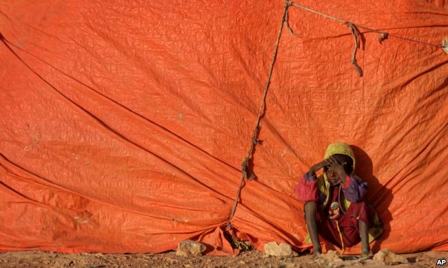 A young Somali boy sits outside his makeshift hut at a camp for people displaced from their homes elsewhere in the country by the drought, shortly after dawn in Qardho, Somalia, March 9, 2017.