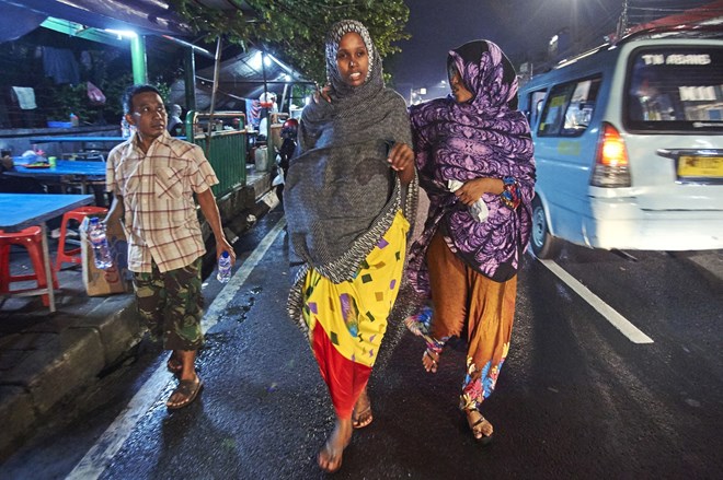 Somalia refugees Norta and Khadro walk at night in a Jakarta street.