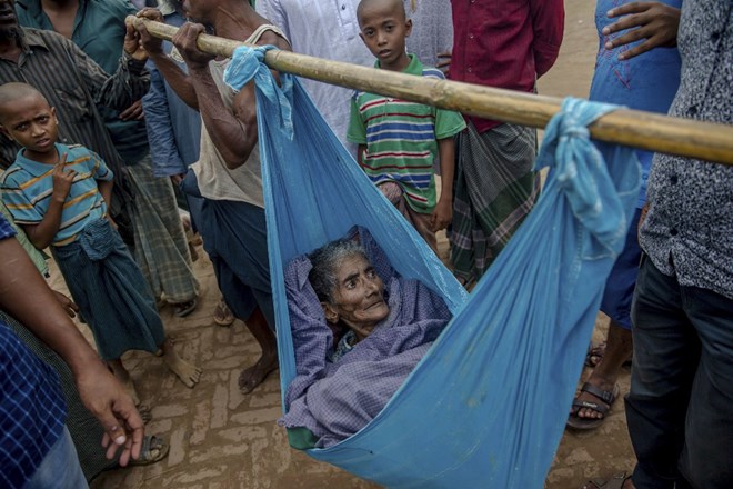 In this Sunday, Jan. 28, 2018, photo, a Rohingya girl holds her brother while standing in front of their makeshift shelter at Jamtoli refugee camp in Cox's Bazar, Bangladesh. Their houses are often made of plastic sheets. Six months after waves of attacks emptied Rohingya villages in Myanmar, sending 700,000 people fleeing into Bangladesh, there are few signs anyone is going home soon. (AP Photo/Manish Swarup)