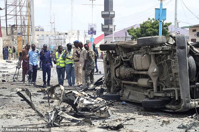 Somali forces watch a vehicle demolished by twin blast in Mogadishu on Saturday, July, 7, 208. At least nine people have been killed and many others injured in an ongoing attack at Somalia's interior ministry as security forces continued battling militants holed up inside, Somali officials say.(AP Photo/Mohamed Sheikh Nor)