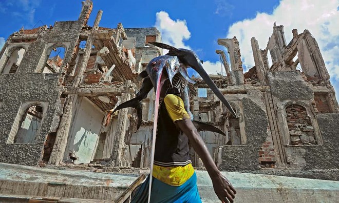 A fisherman carries a sailfish past buildings destroyed in the warfare. Photograph: Mohamed Abdiwahab/AFP/Getty Images